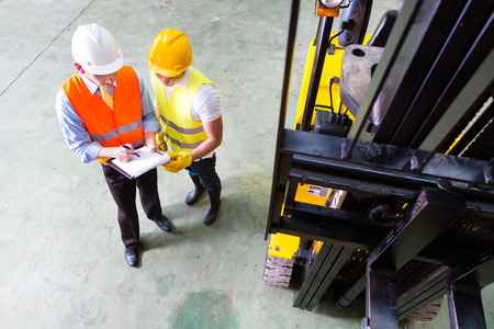 fork lift truck driver discussing checklist with foreman in warehouse